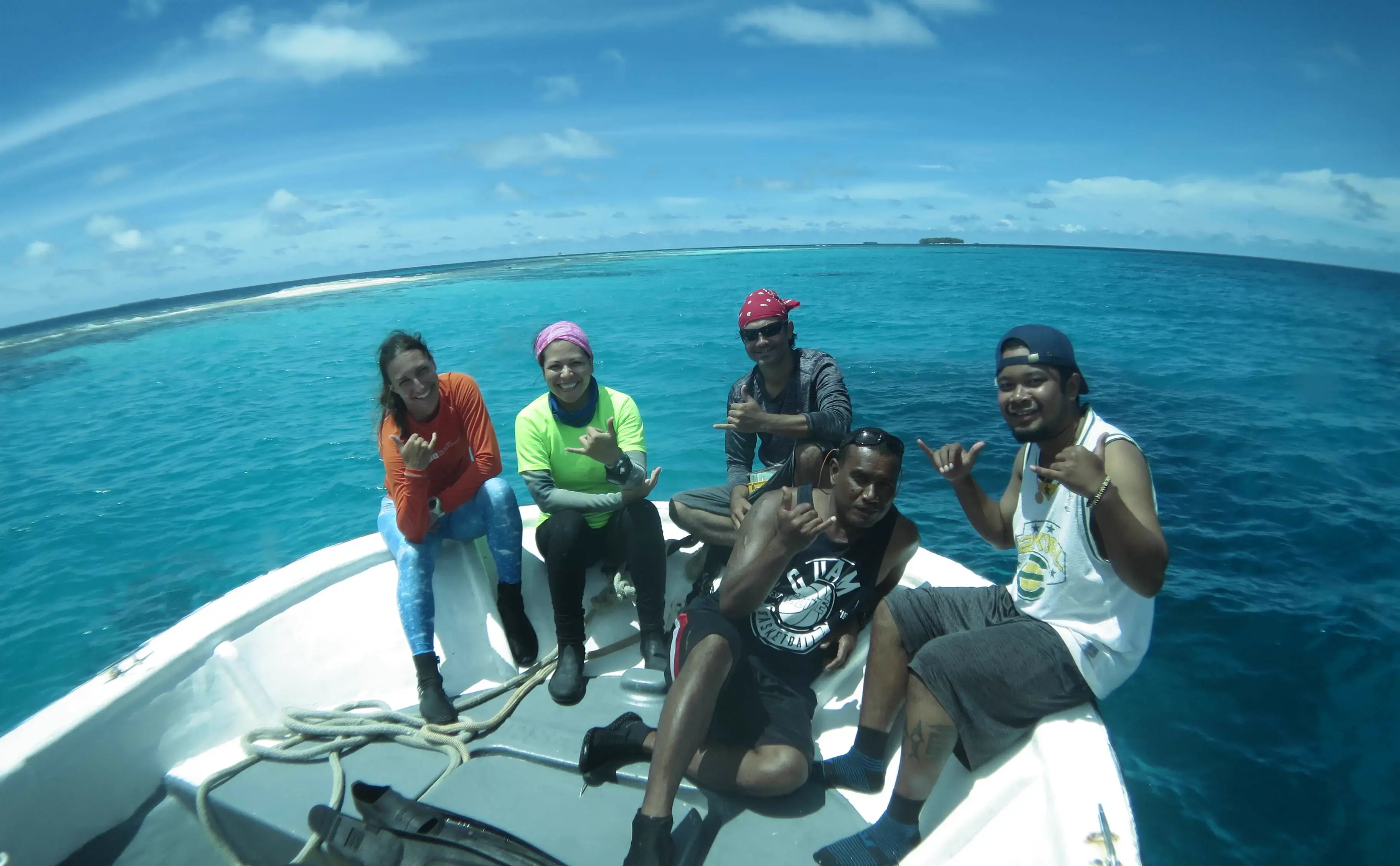 A group of five diverse marine researchers smiling on a boat in tropical waters.